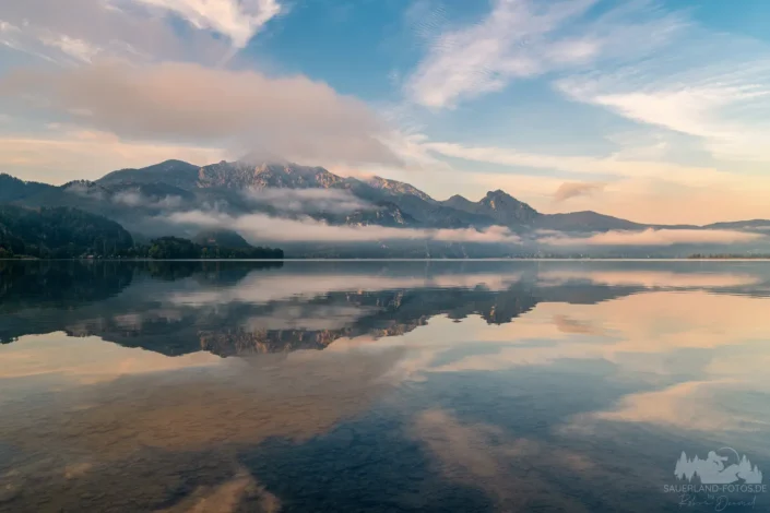 Walchensee in Bayern mit spiegelnden Bergen, tief liegenden Nebelbändern und pastellfarbenem Himmel bei Sonnenaufgang
